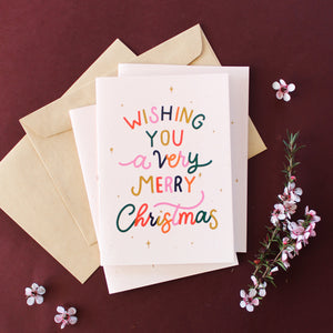 Wishing You a very Merry Christmas in colourful lettering surrounded by merry little stars, set against a blush background