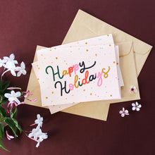 Load image into Gallery viewer, &#39;Happy Holidays&#39; in colourful lettering surrounded by confetti and merry little stars, set against a blush background.