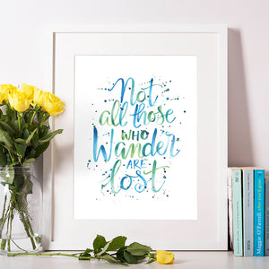 Not All Those Who Wander Are Lost - J R R Tolkein hand lettered quote in modern calligraphy style using hues of blue and green with paint splatters